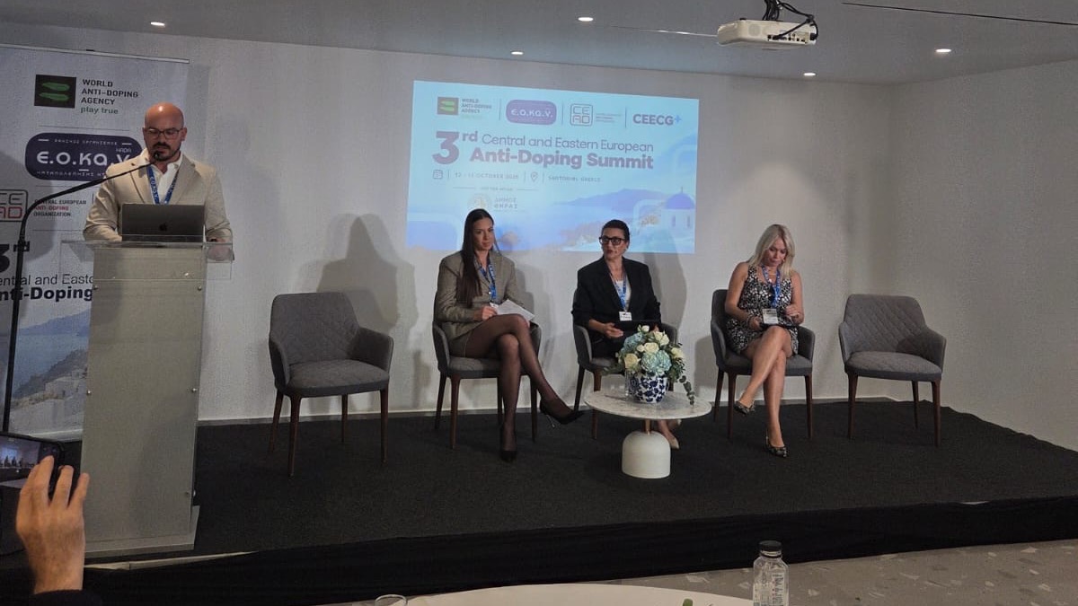 Moderátor pri rečníckom pulte a tri panelistky na pódiu antidopingového summitu na Santorini.
